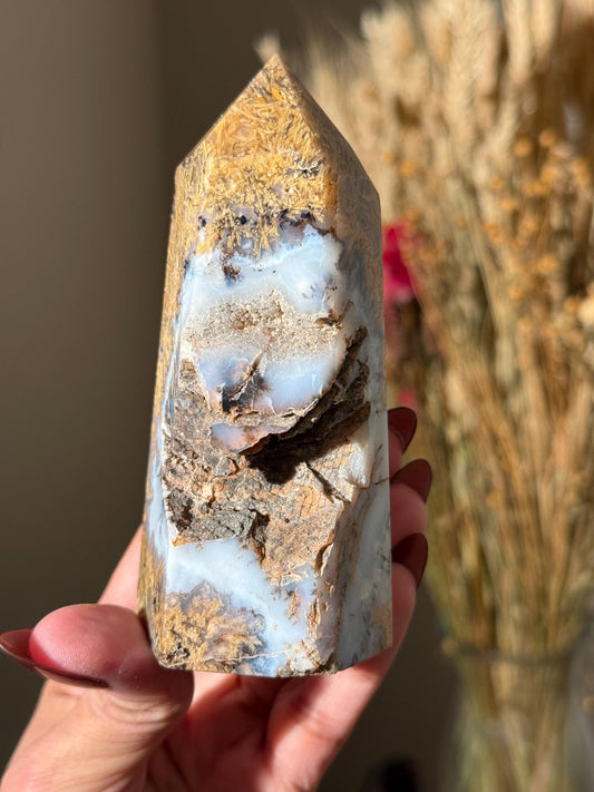 May include: A brown, white, and gray agate crystal point with a pointed top and a flat base. The crystal has a unique pattern of swirls and lines.
